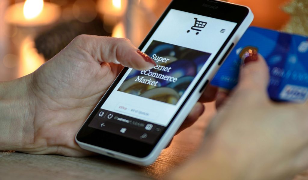Woman using smartphone for online shopping with credit card in hand, festive background lighting.